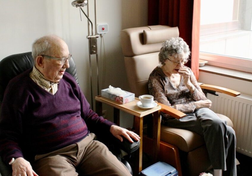 Elderly couple sitting in armchairs with tea and biscuits